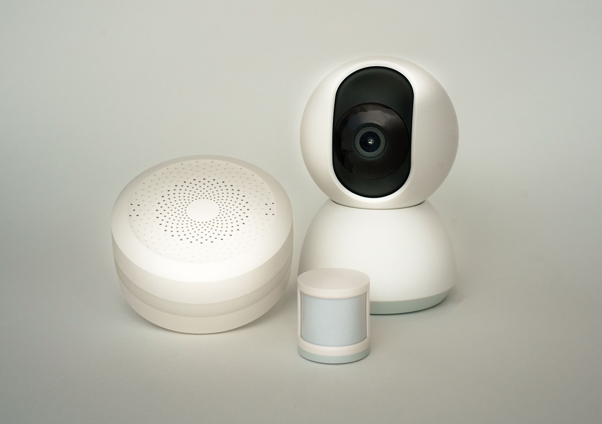 Detector de movimento, central de alarme com sirene e câmara interior, todos brancos, sobre fundo cinzento
